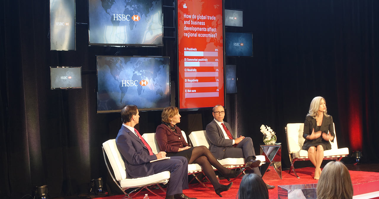 4 people sitting on stage talking to the audience. A screen behind them shows a live multiple choice question.