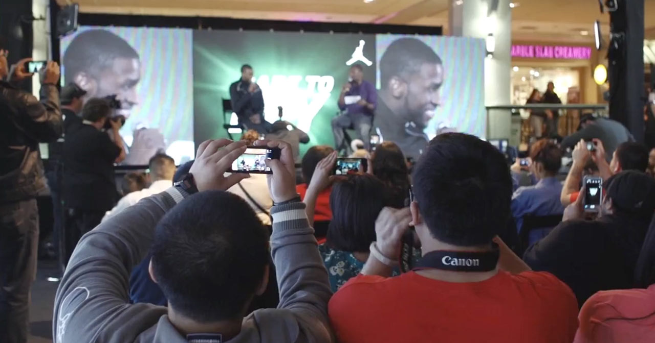 Crowd holding phones up to photograph or record NBA players being interviewed on stage.