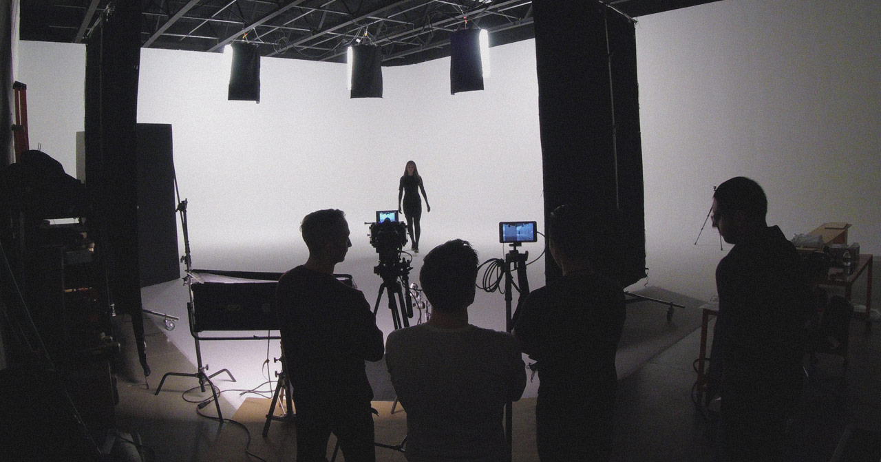 Four people behind cameras watching actress walk towards the camera.