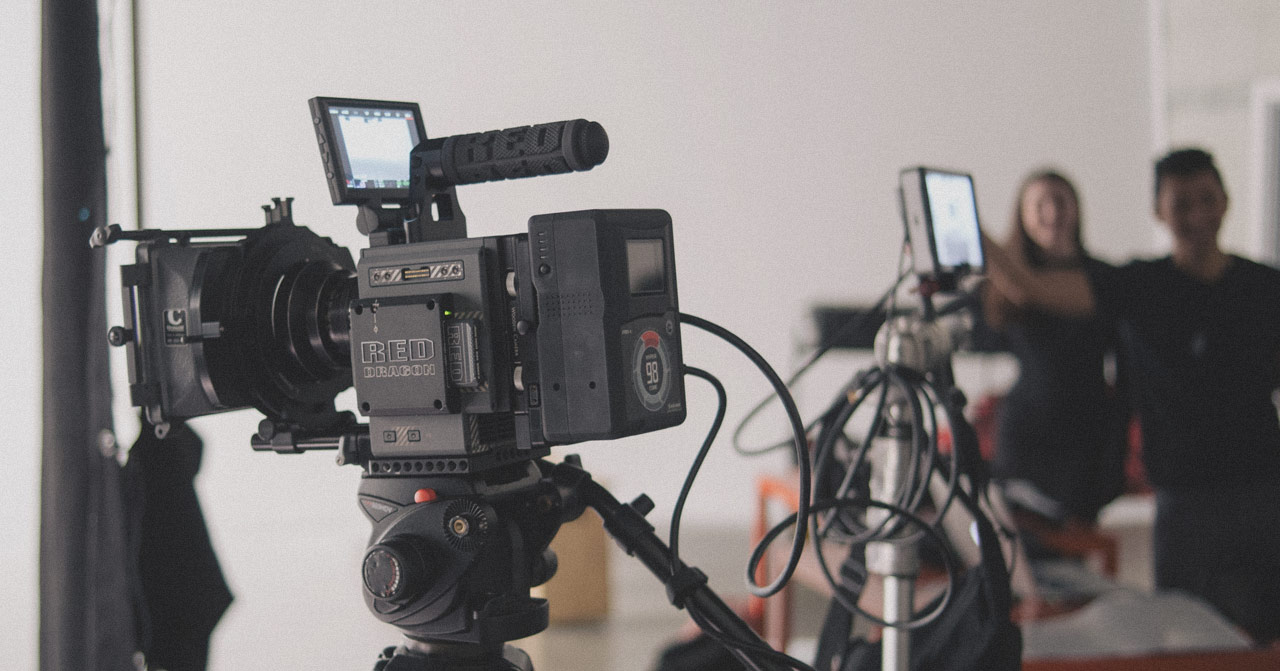 Shot of a video camera with two people blurred in the background.