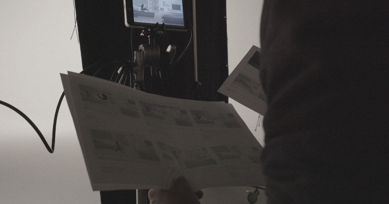 Close up of a person shuffling through pages of a storyboard with a screen in front of them.