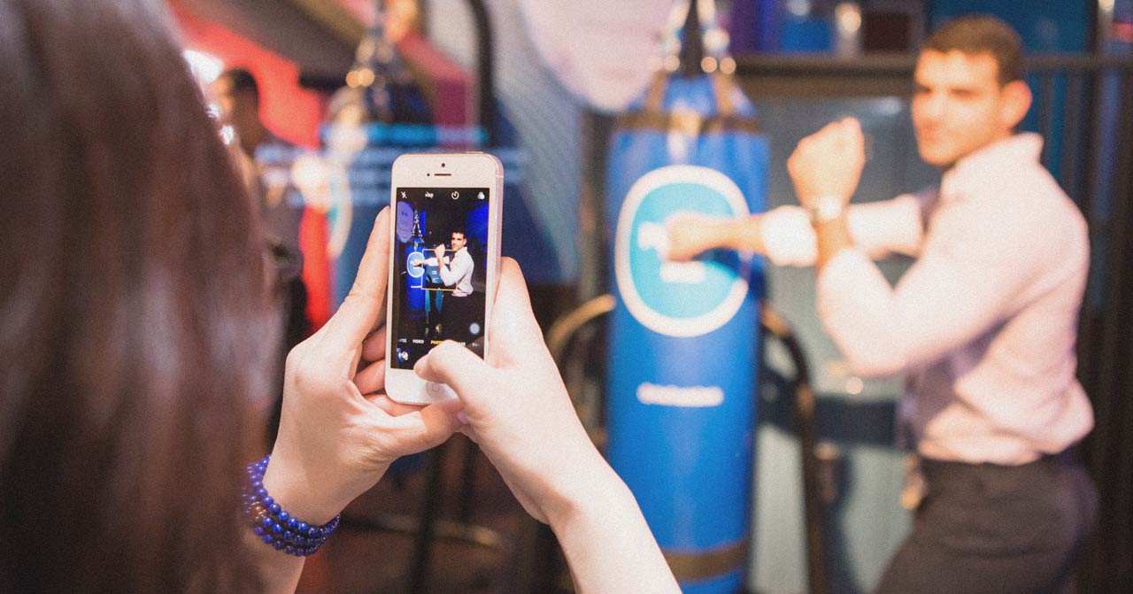 Woman photographs a man posing in front of a punching bag